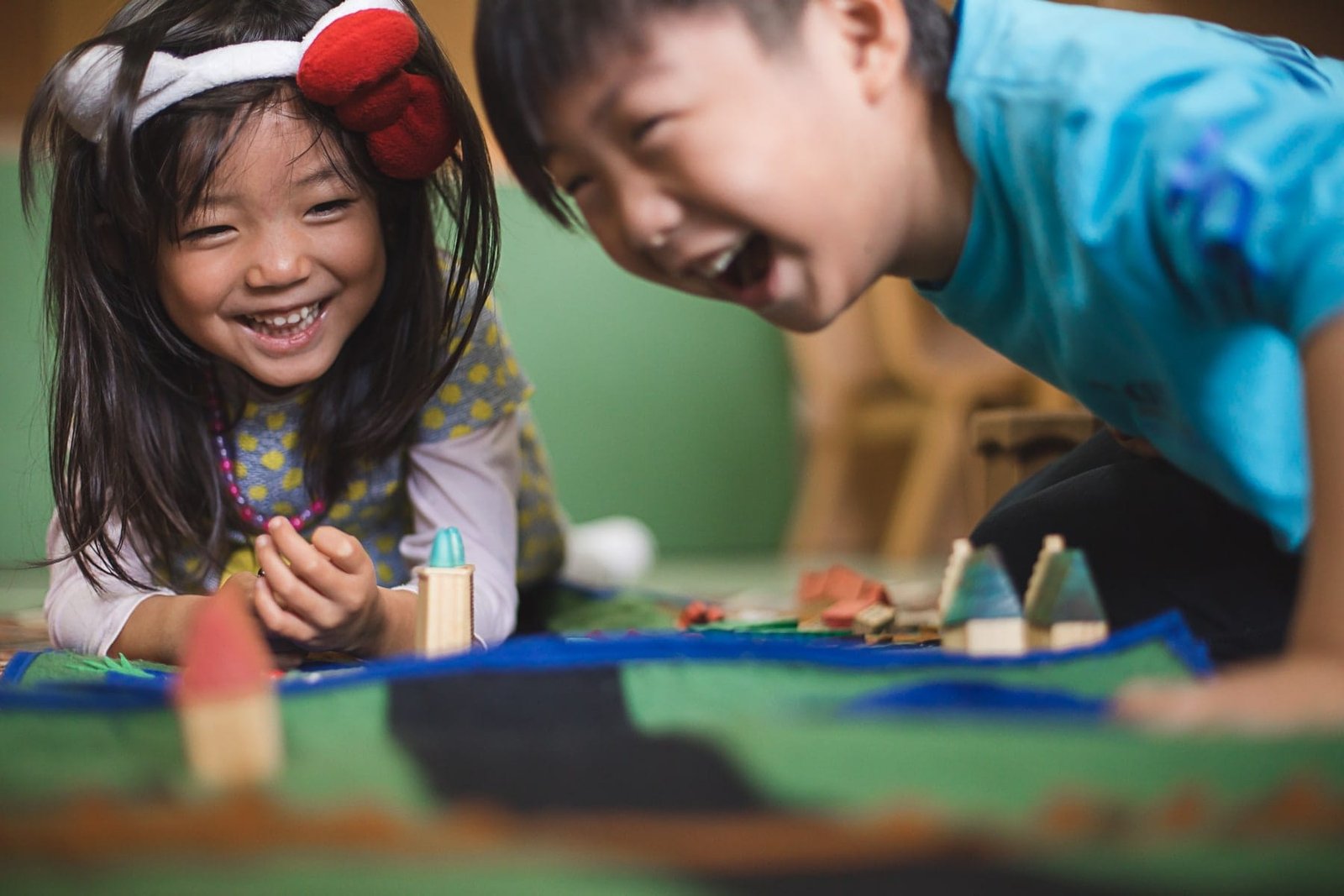 Dos niños orientales sonriendo mientras juegan en el suelo con materiales Montessori en la escuela Bloom