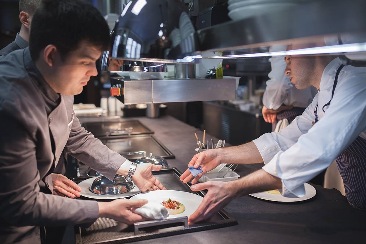 Cocinero dándole un plato con comida a un camarero para que lo sirva en la cocina del restaurante seta